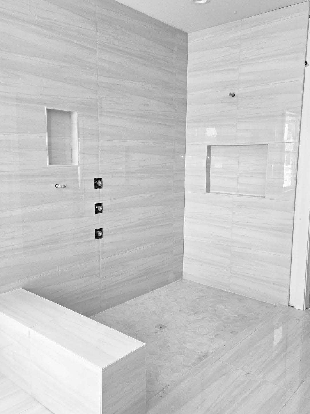 Modern shower with light-colored tile walls, built-in bench, and recessed shelves.