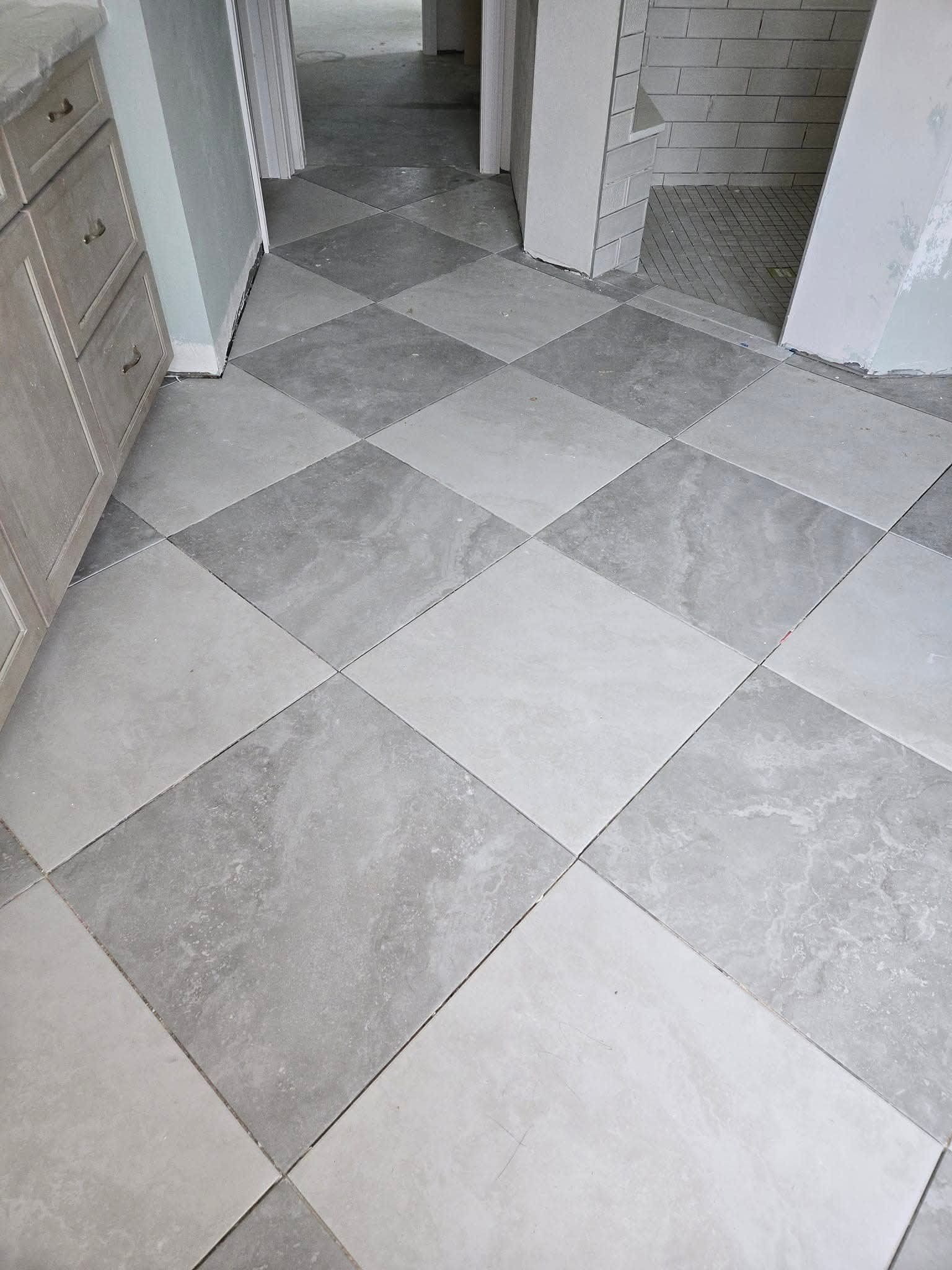 A checkerboard pattern floor made of light and dark gray tiles. Kitchen cabinets on the left, doorway in the background.