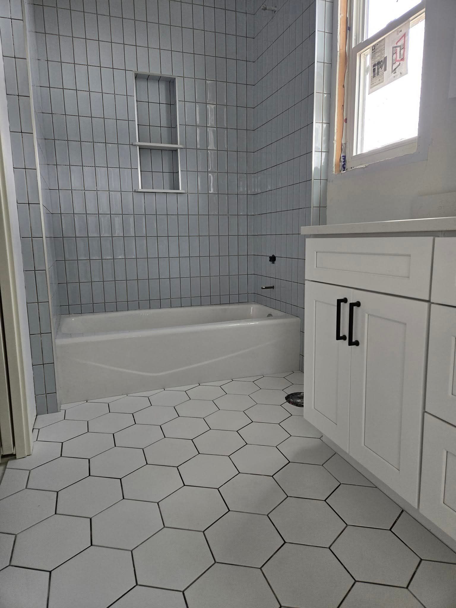 Newly renovated bathroom with white hexagon floor tiles, blue and white shower wall tiles, and white vanity.