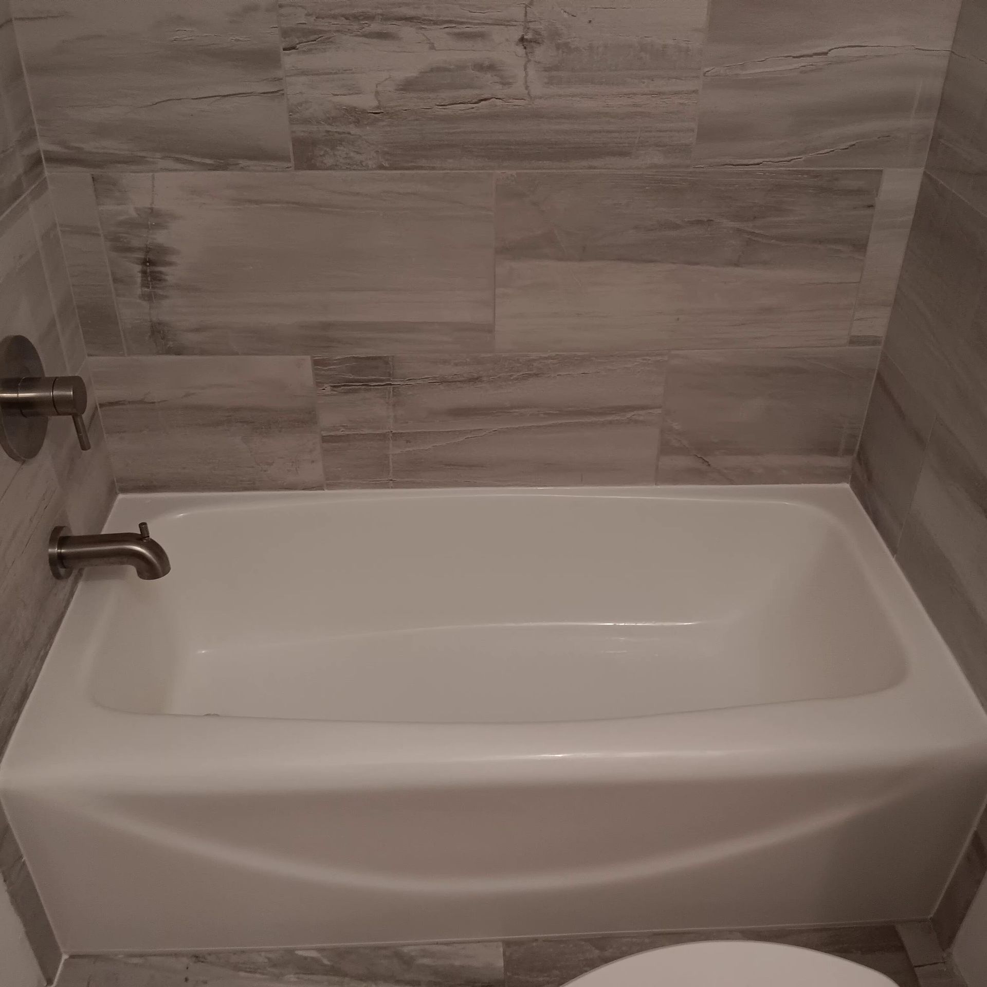 White bathtub with silver faucet, set against gray tiled wall in a bathroom.