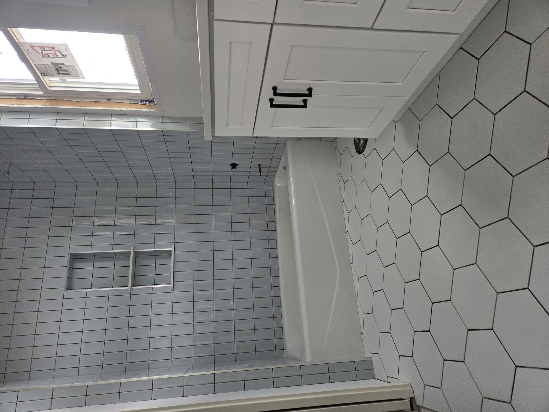 Bathroom with white honeycomb tile floor and rectangular wall tiles. A white vanity hangs above the tub.