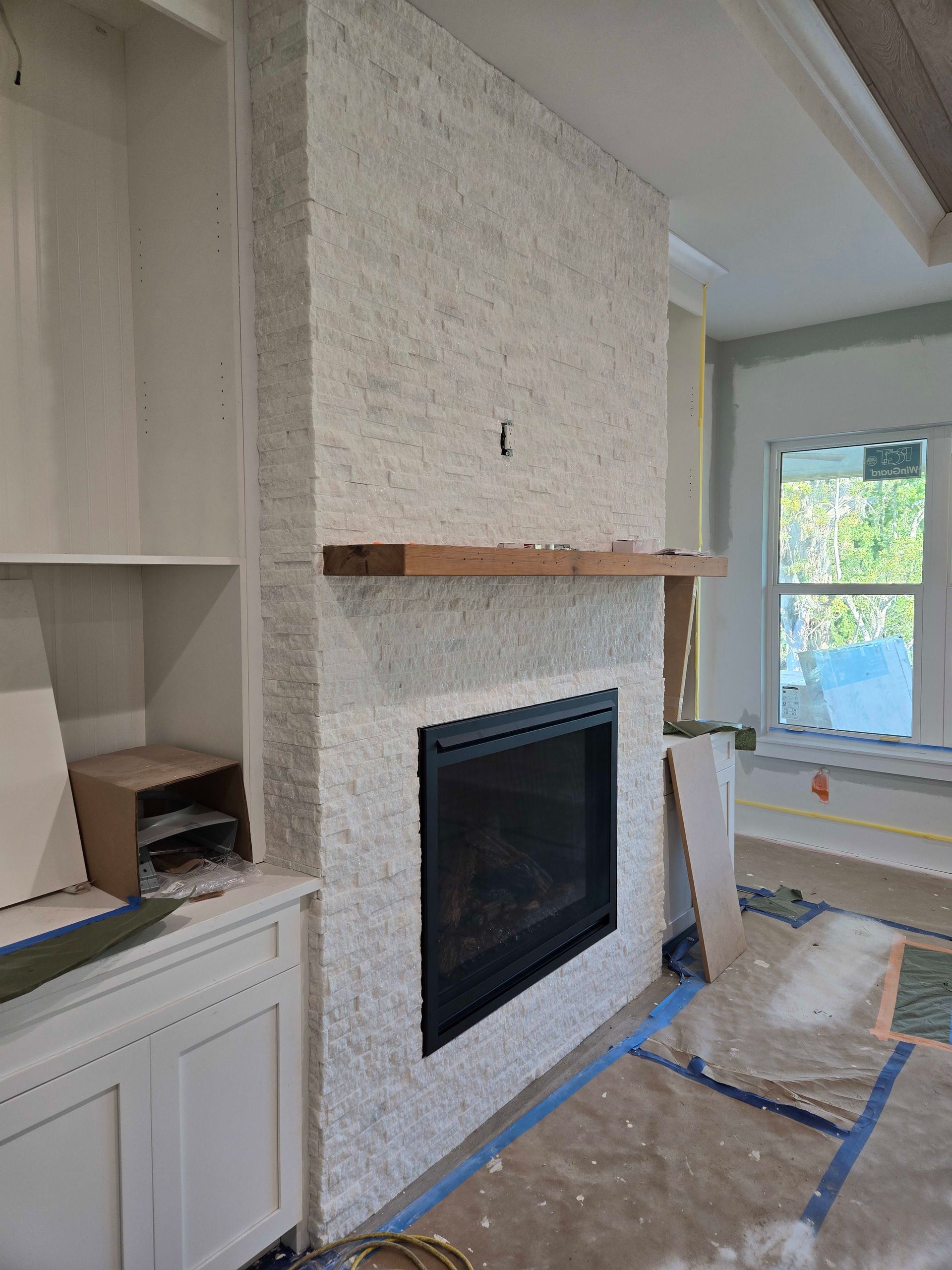 Fireplace with light stone facing, black firebox, wooden mantel, and built-in white shelving.