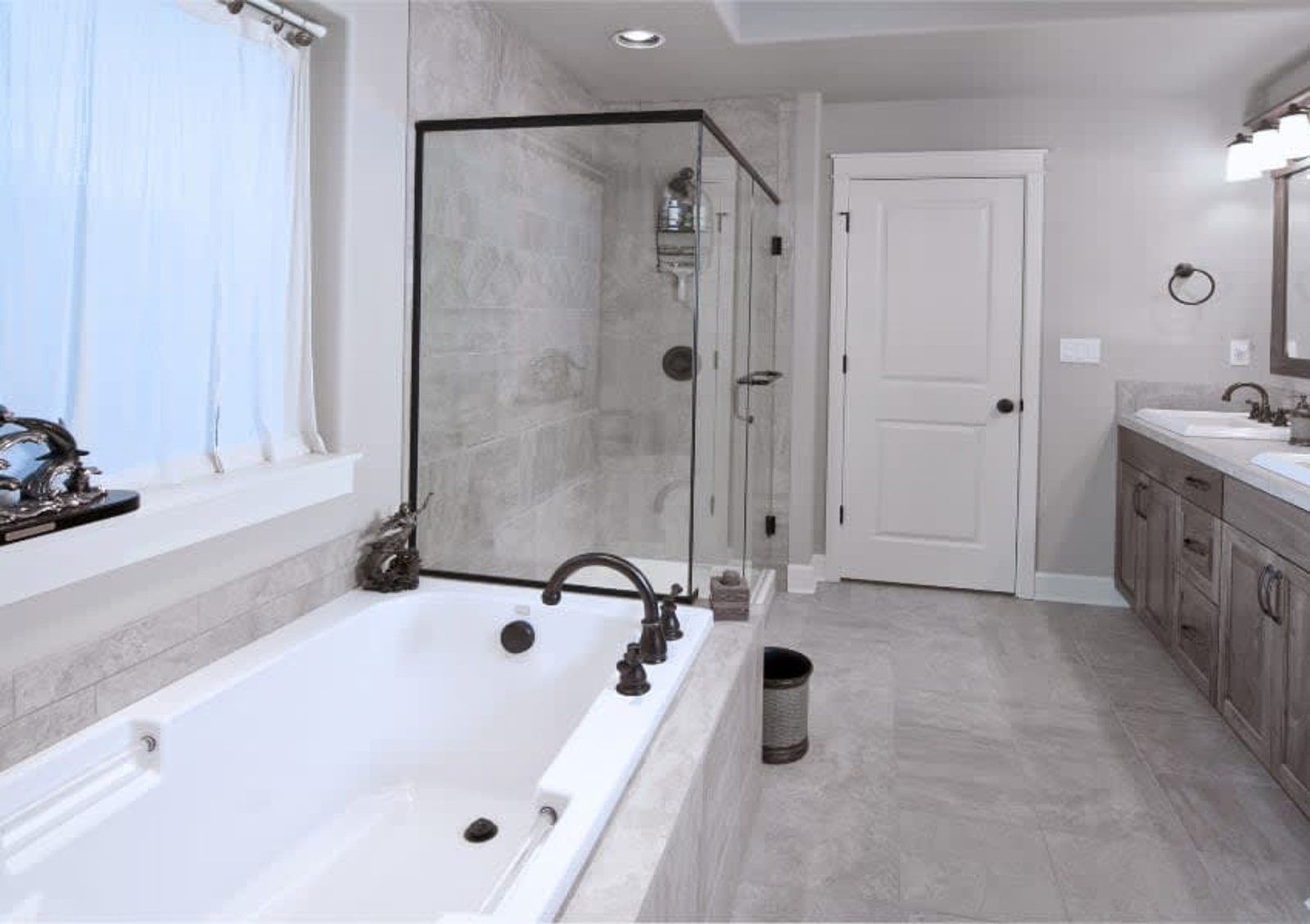 Bathroom with a white bathtub, glass shower, and gray walls, with a double sink vanity.