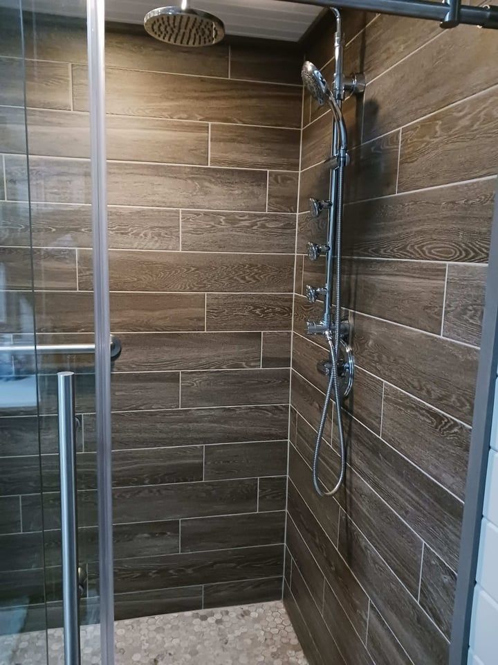 Shower with brown wood-look tiles, glass door, and multiple showerheads.