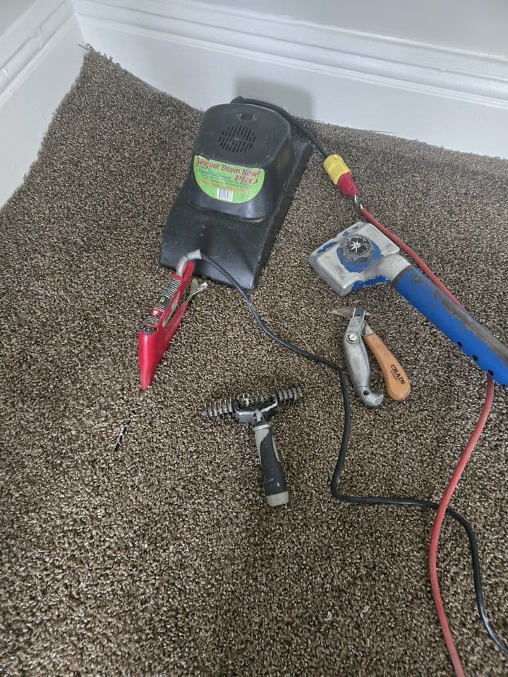 Tools for carpet installation on brown carpet: stretcher, cutter, pliers, seam iron.