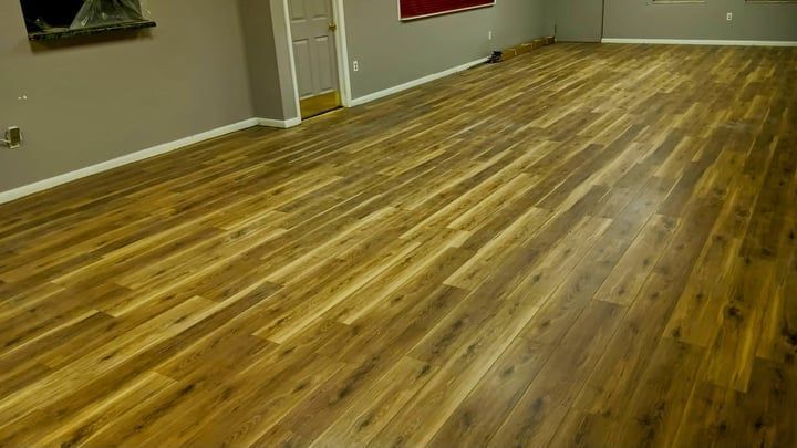 Hardwood floor in an empty room, golden brown planks, gray walls, white baseboard, door.