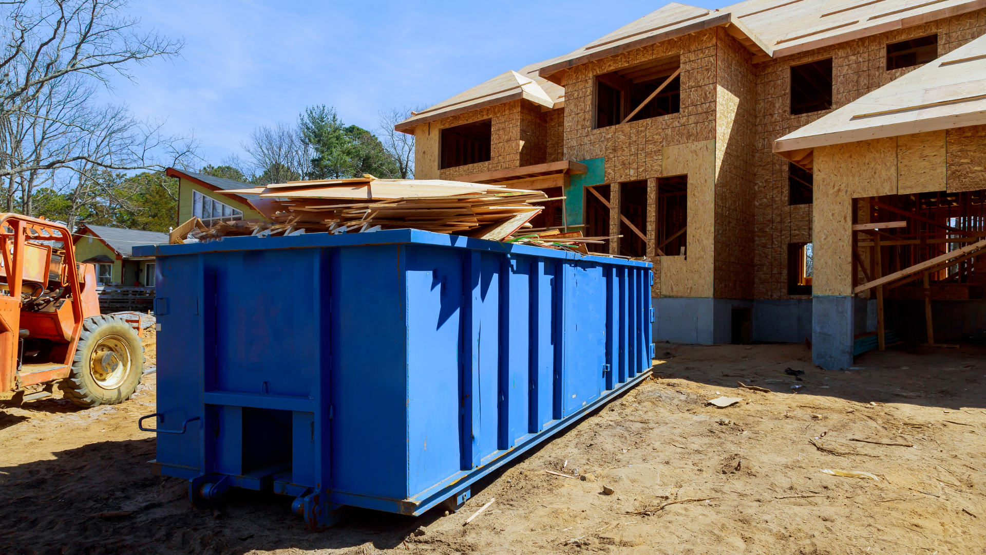 Blue dumpster in front of a partially built house at a construction site