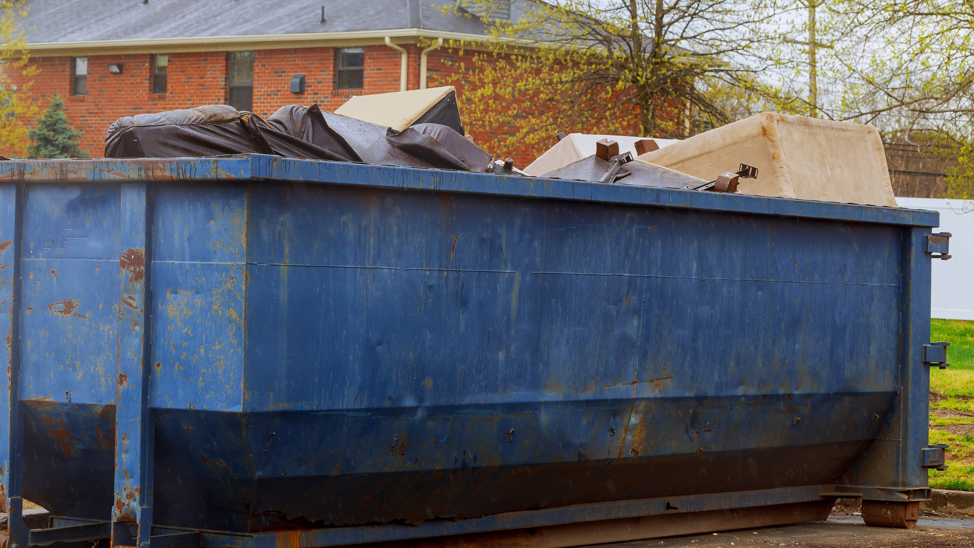Blue dumpster filled with trash and debris beside a brick building