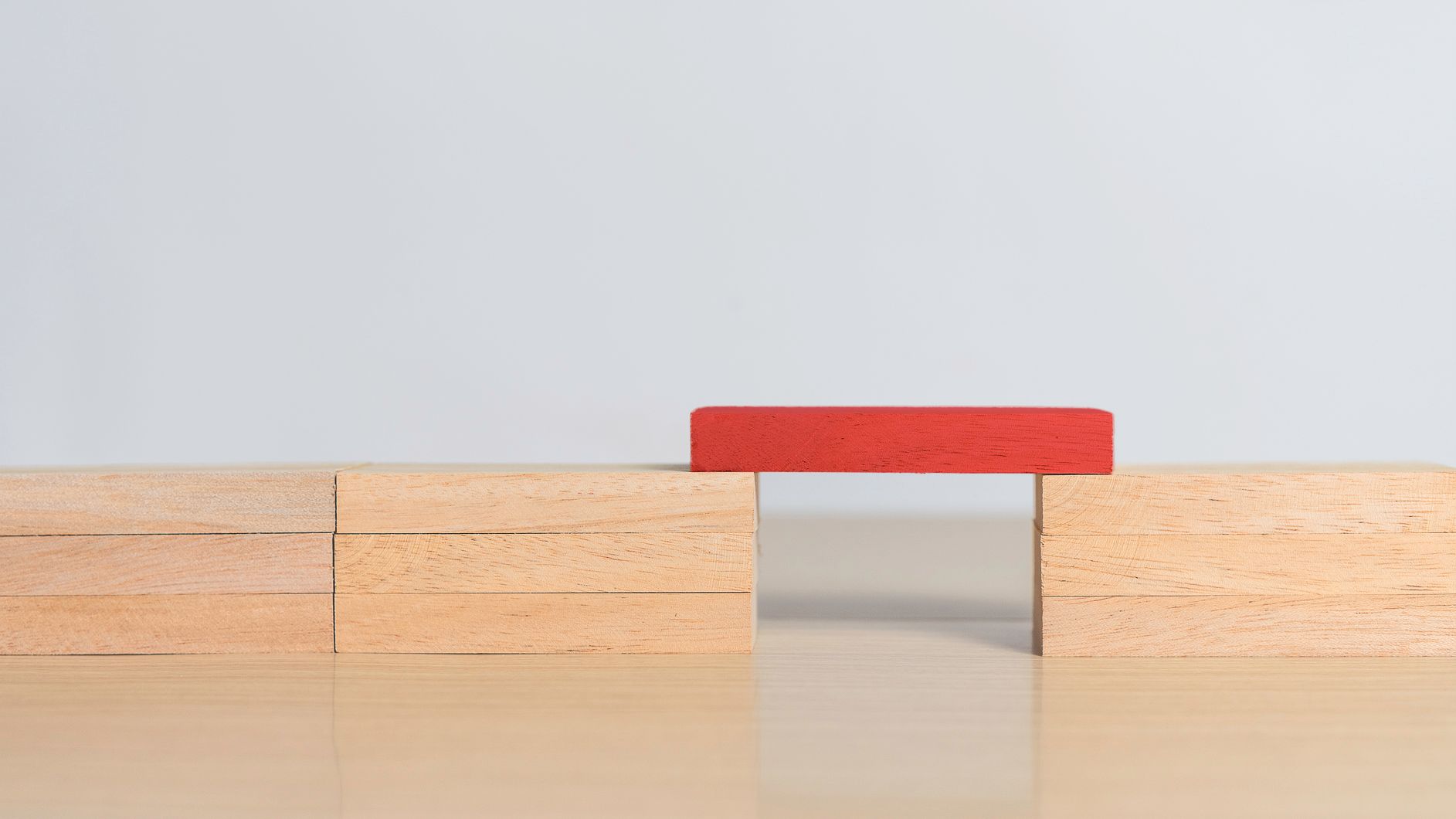 Red block bridging two stacks of wooden blocks on a light surface.