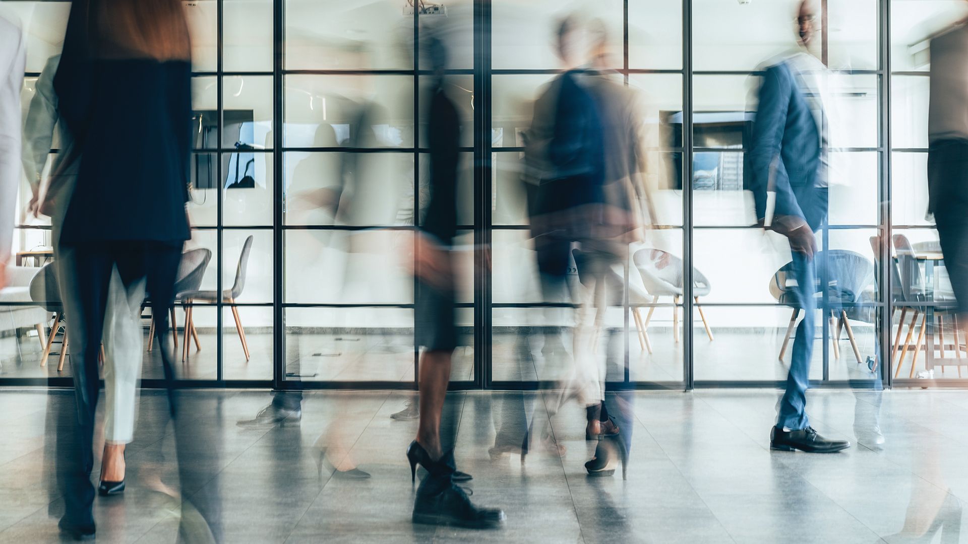 Blurred figures walk through a glass-walled corporate lobby.