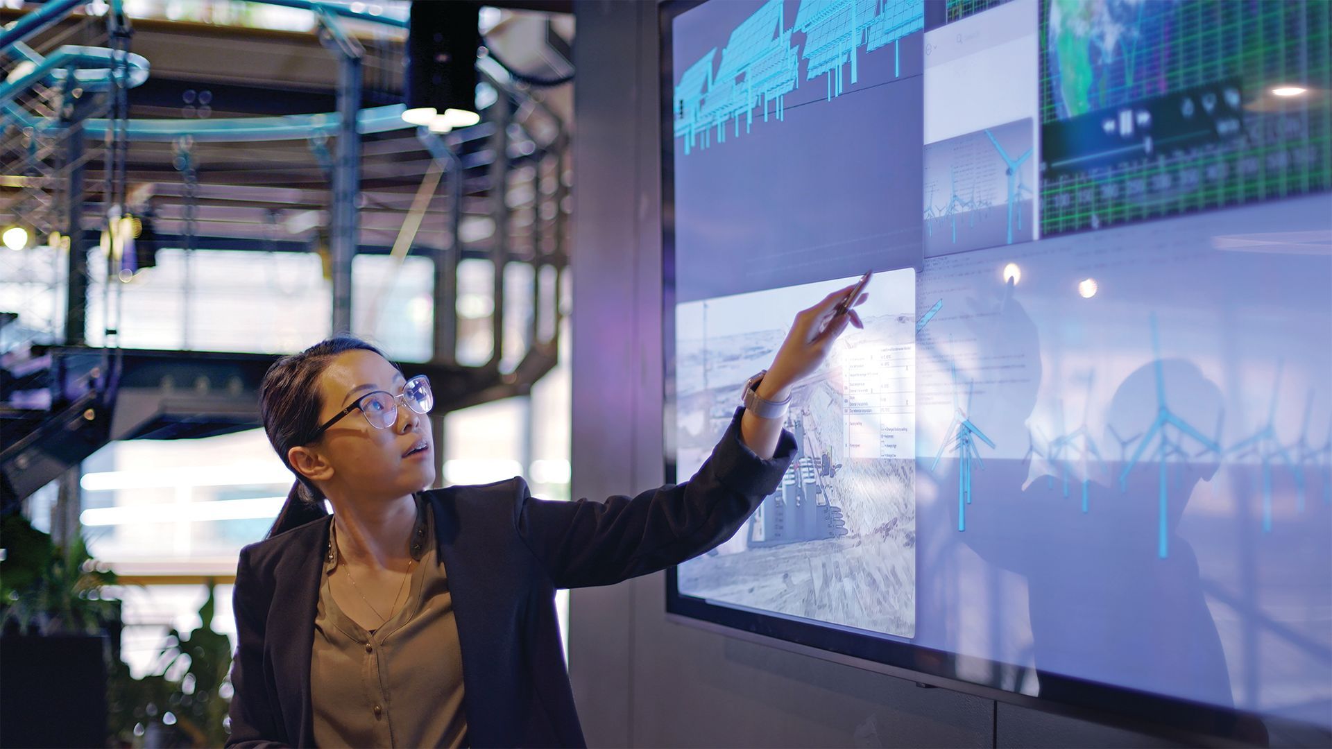 Professional woman points to glowing screen which displays a range of graphs and information.