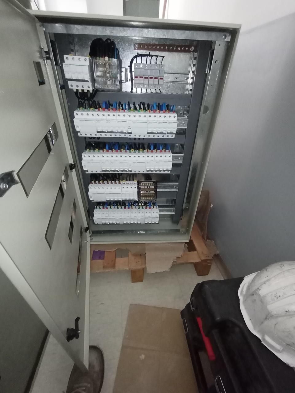 Panel eléctrico abierto con disyuntores y cableado. Dentro de una habitación con casco y maletín negro.