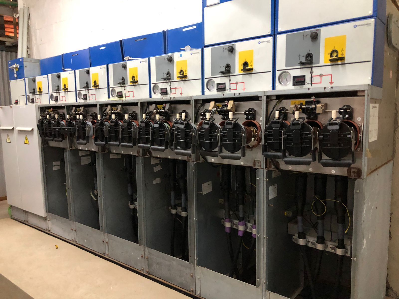 Tablero eléctrico con múltiples interruptores automáticos negros en un gabinete metálico gris y azul.