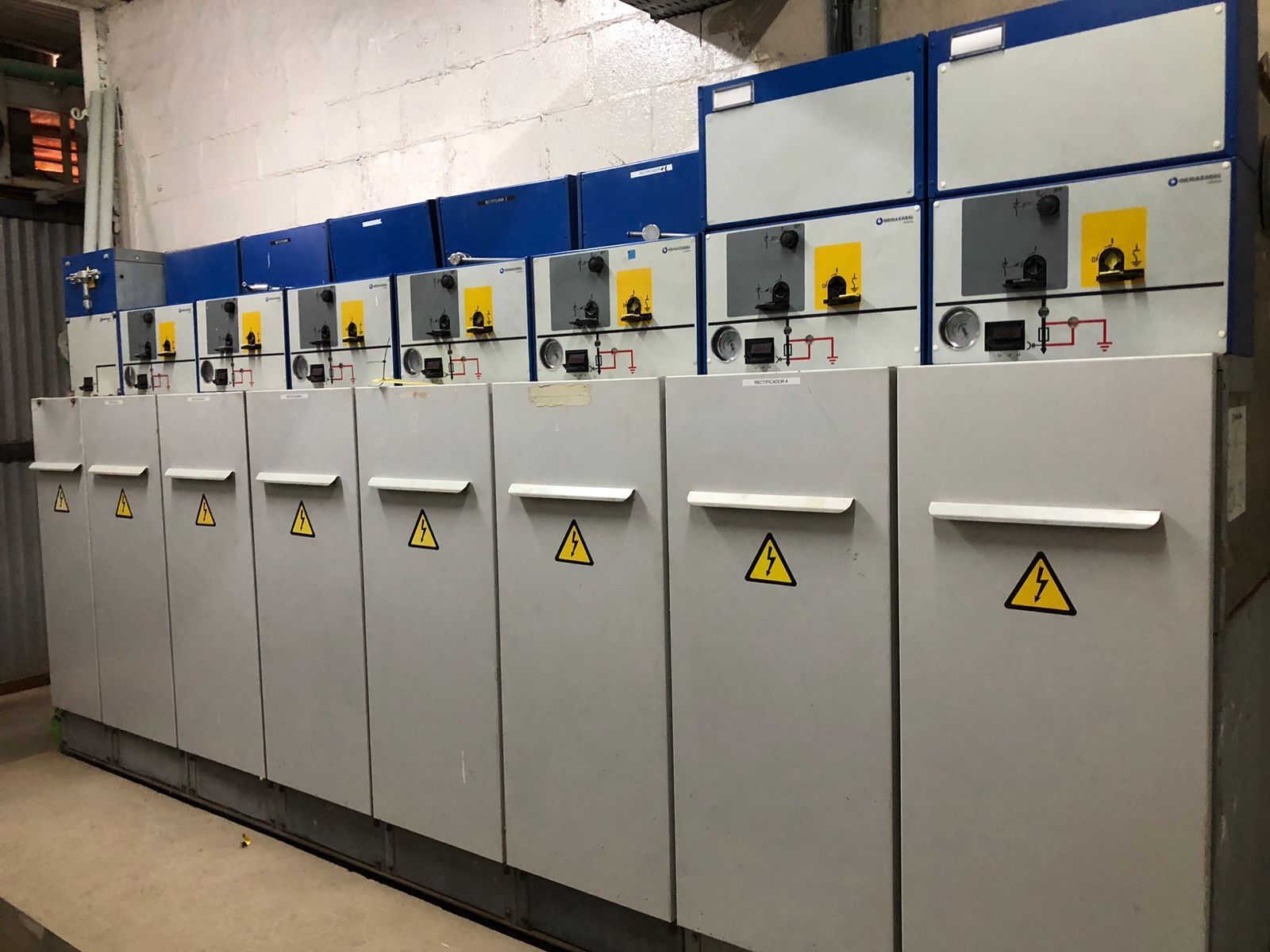 Armarios de distribución eléctrica con tapas azules y símbolos de peligro amarillos.