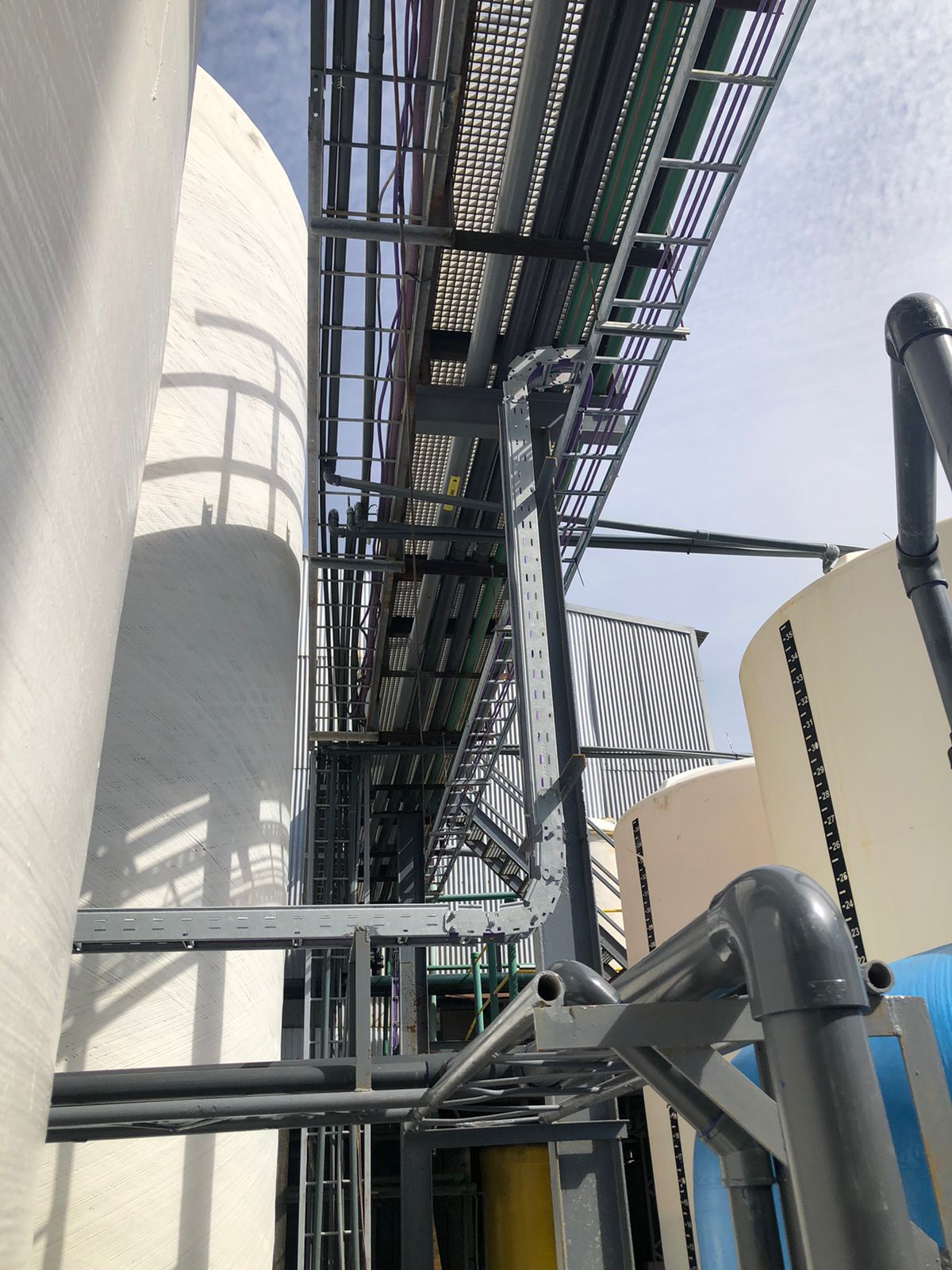 Infraestructura industrial con tanques, tuberías y una pasarela bajo un cielo azul.