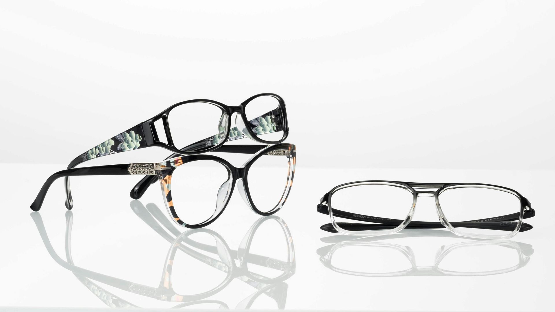 Tres pares de gafas sobre una superficie blanca reflectante: dos apilados, uno a un lado.