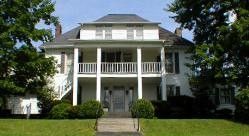 White two-story funeral home with porch and columns, dark roof, set on a green lawn.