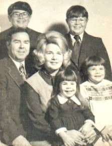 Family portrait: Six people, smiling, posing together, possibly indoors.