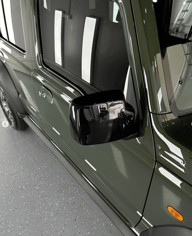 A black suzuki suv is parked in a garage for ceramic coating on side mirrors