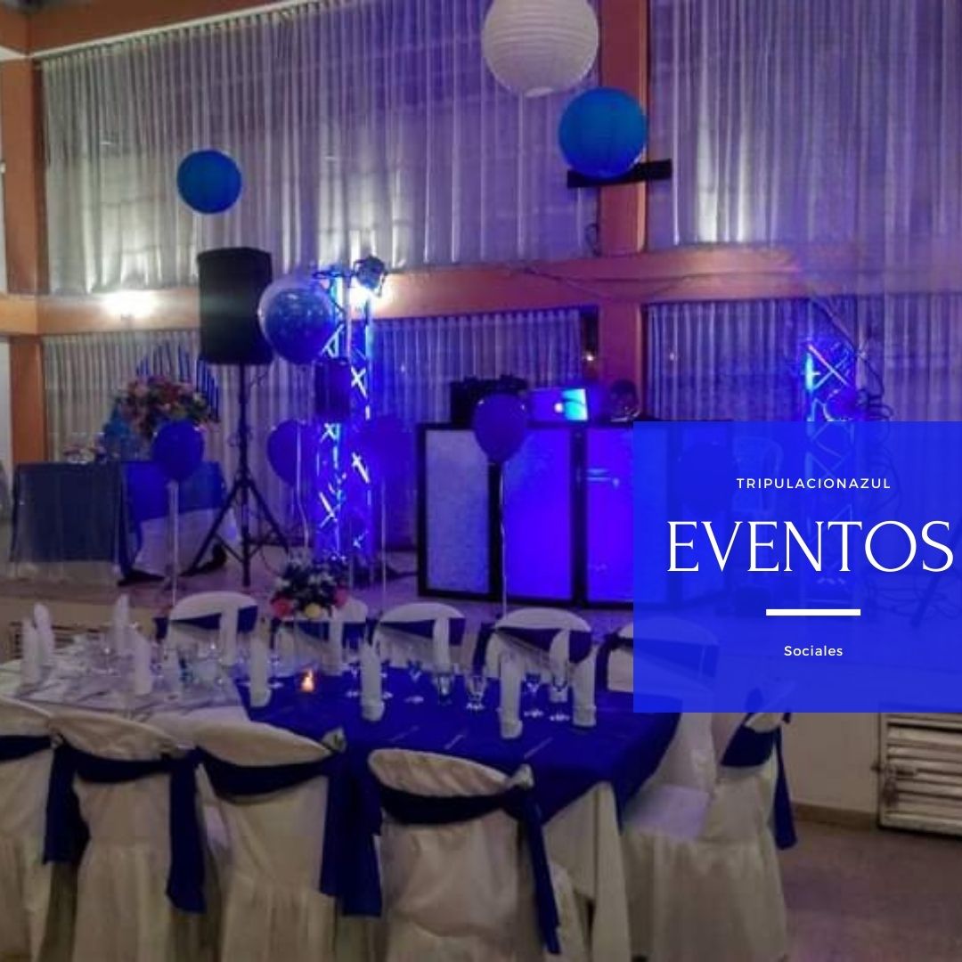 Salón de eventos decorado en azul con mesas, sillas y equipo de DJ. Globos y faroles cuelgan del techo.