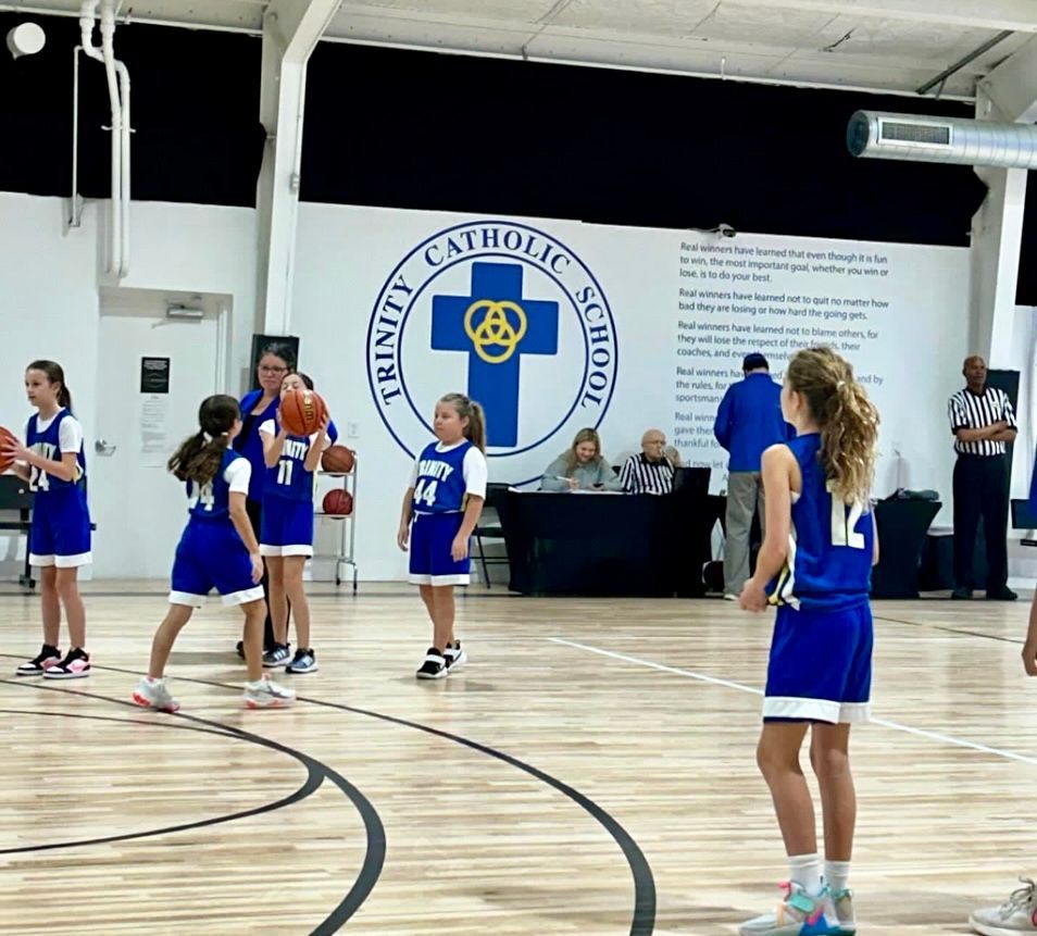 a group of young girls are playing basketball in a gym that says trinity catholic school
