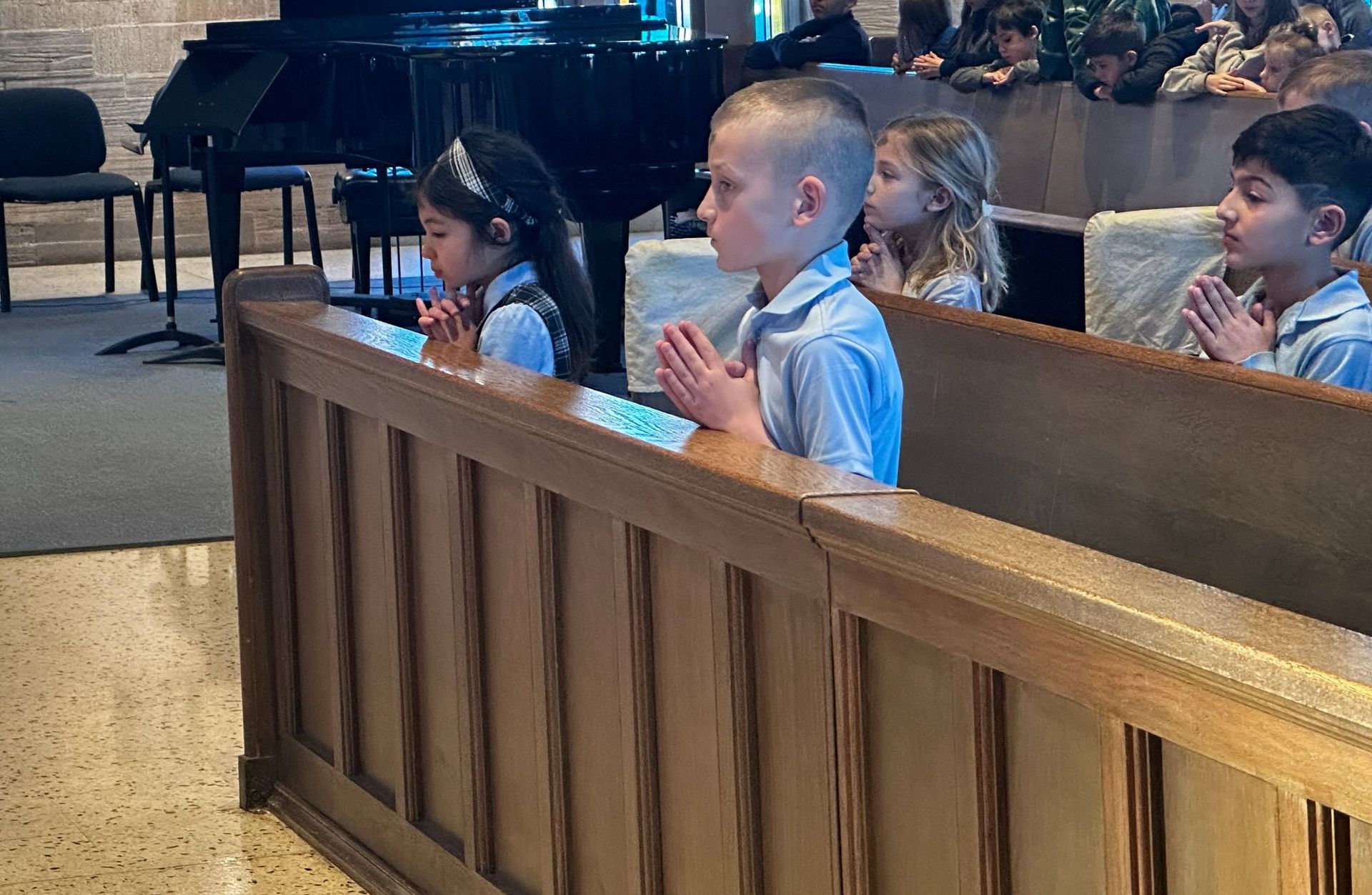 a group of children are praying in a church with a piano in the background .