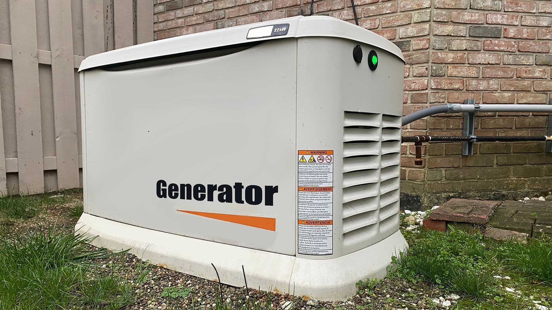 A generator is sitting in the grass next to a brick wall.