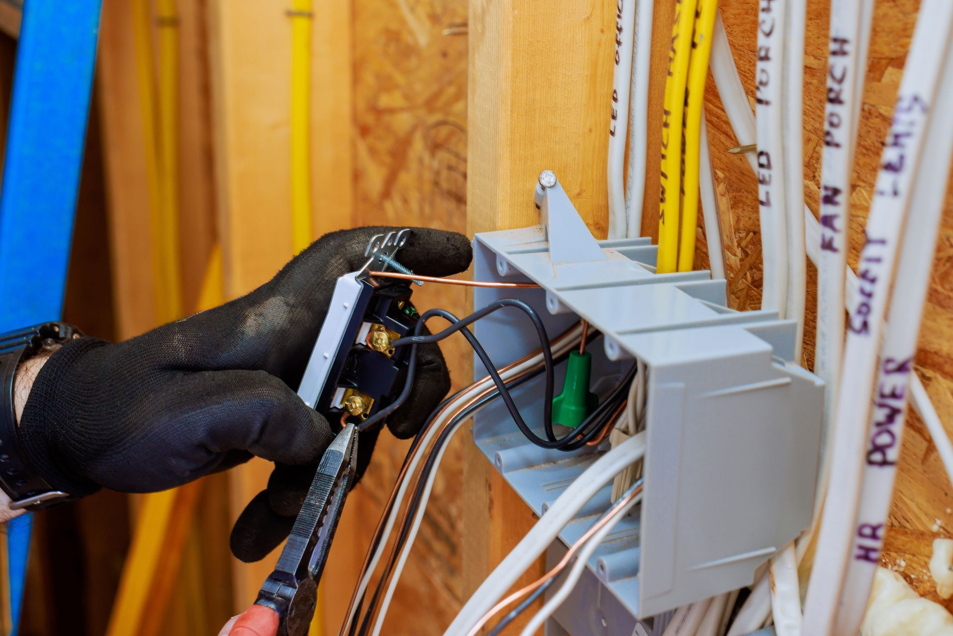 Electrician in black gloves wiring electrical outlet box.