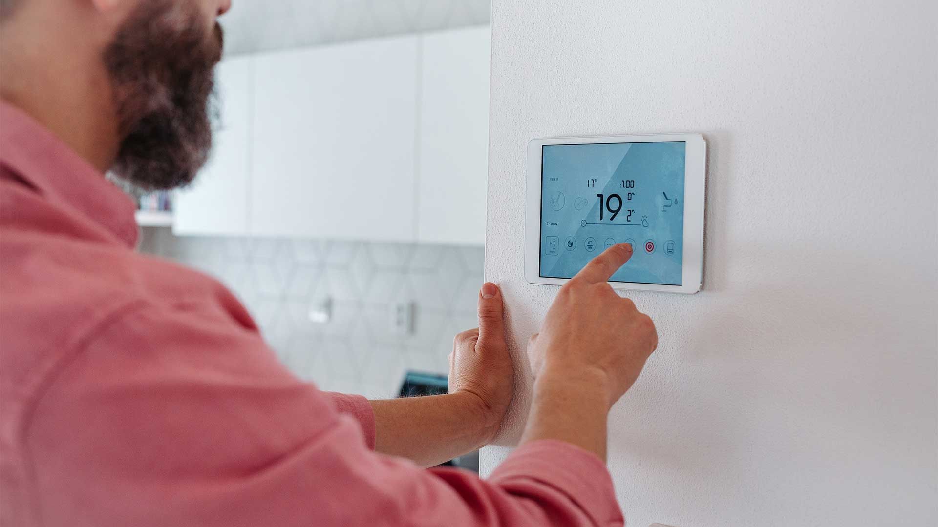A man is using a tablet to control a thermostat on a wall.