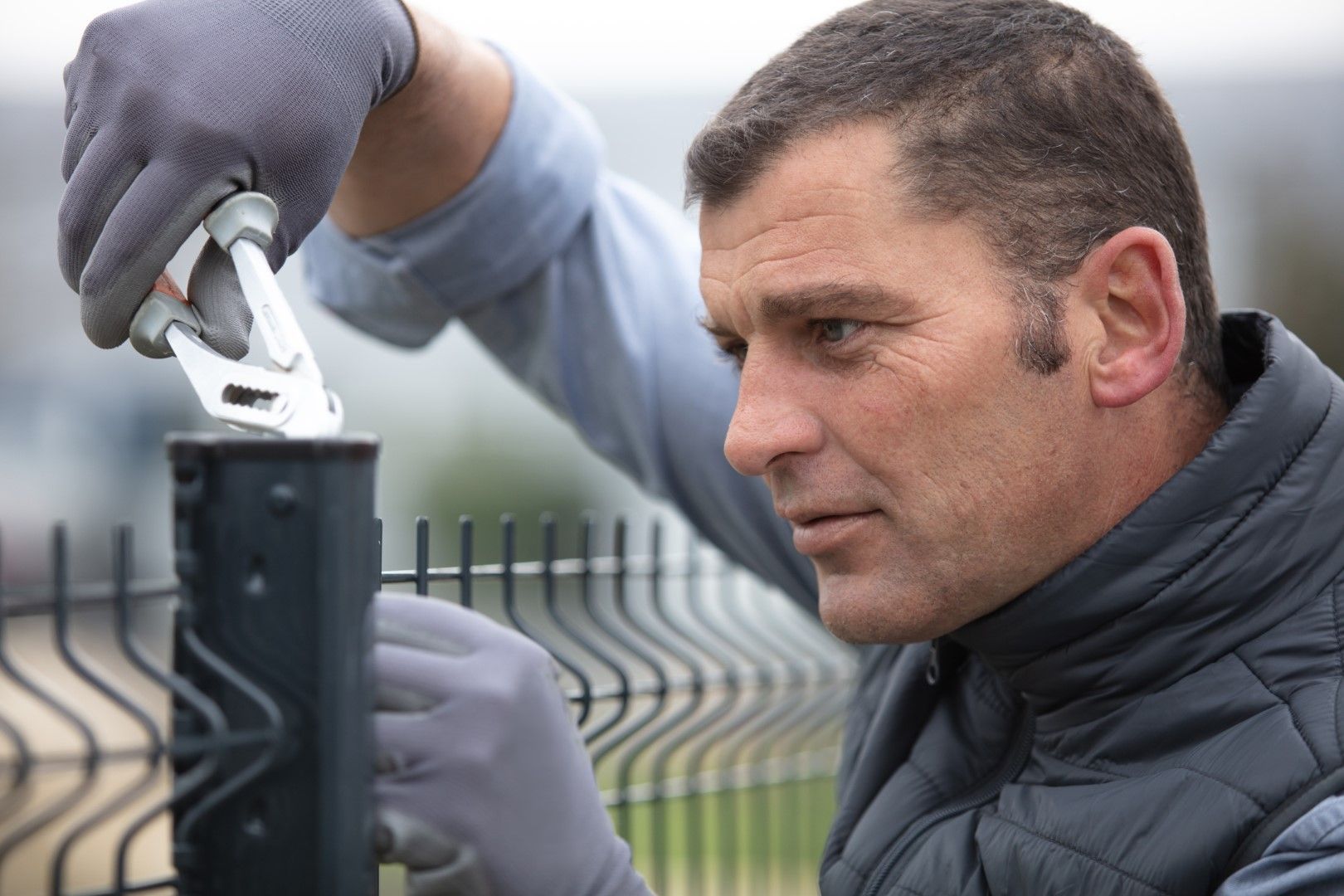 Man in gray gloves using pliers to install fence.