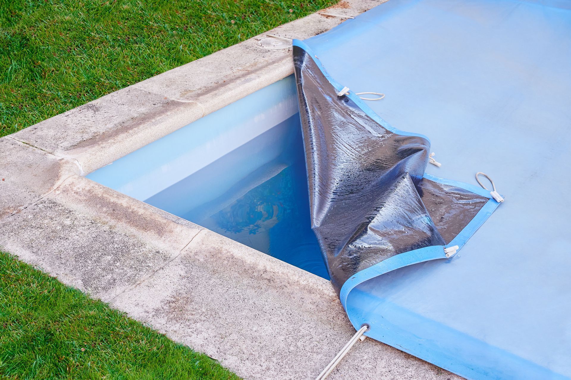 A partially open swimming pool cover rolled back, showing blue water inside a concrete pool area