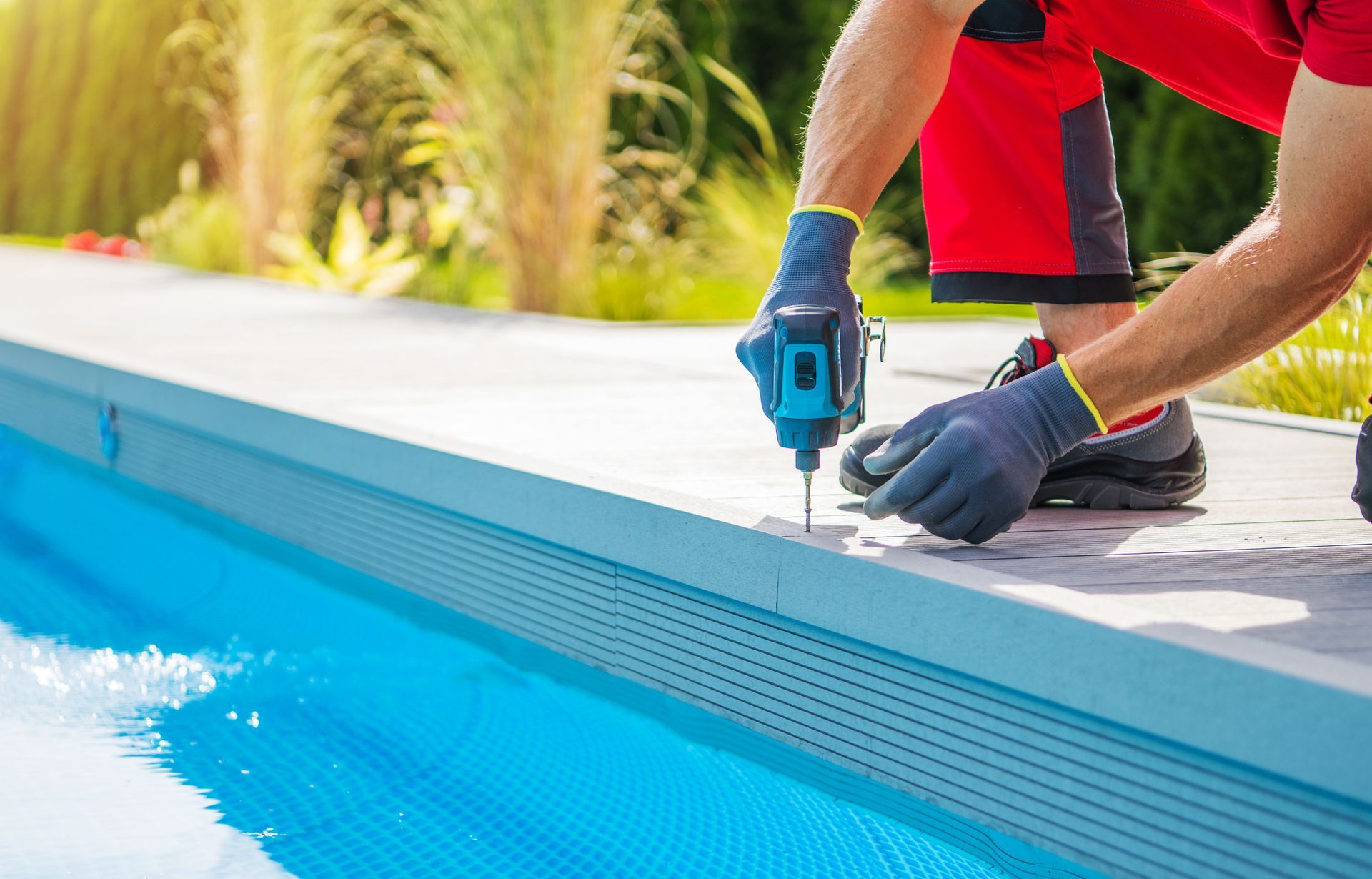 A man wearing a red shirt and gloves uses a drill for residential pool repair by Anchor Pools & Spas