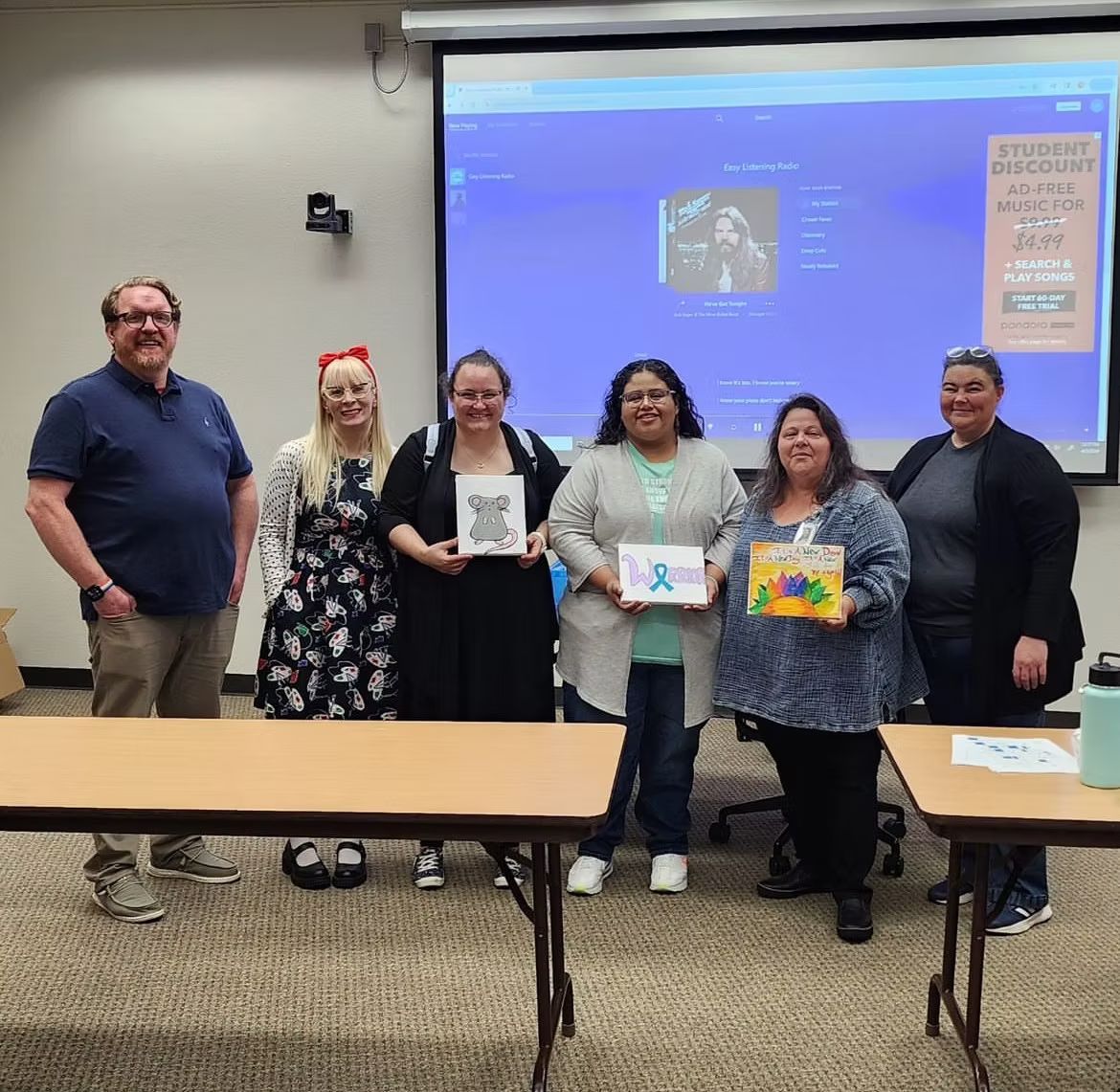 Group of people standing in front of a projection screen, holding books and artwork.