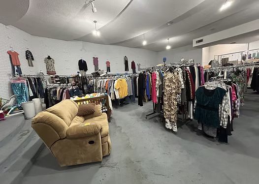 Inside a clothing store, racks of clothes, a recliner, and various items on sale.