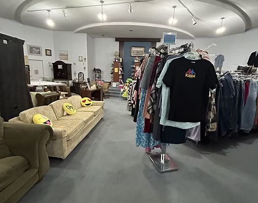 Inside of a thrift store with clothing racks and furniture on display.