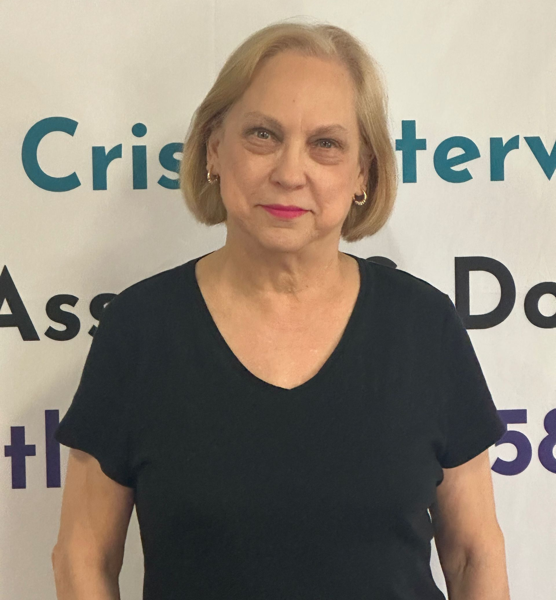 Woman with blonde hair wearing a black shirt, posing in front of a sign.