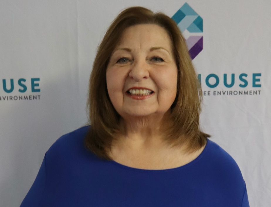 Woman in blue shirt smiles in front of a backdrop with a logo.