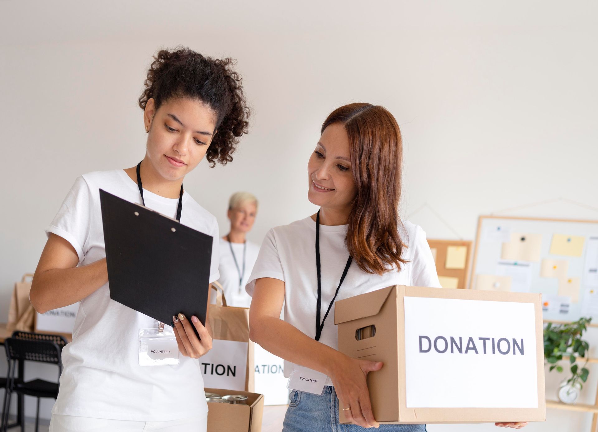 Two women volunteers reviewing a checklist, holding a donation box.