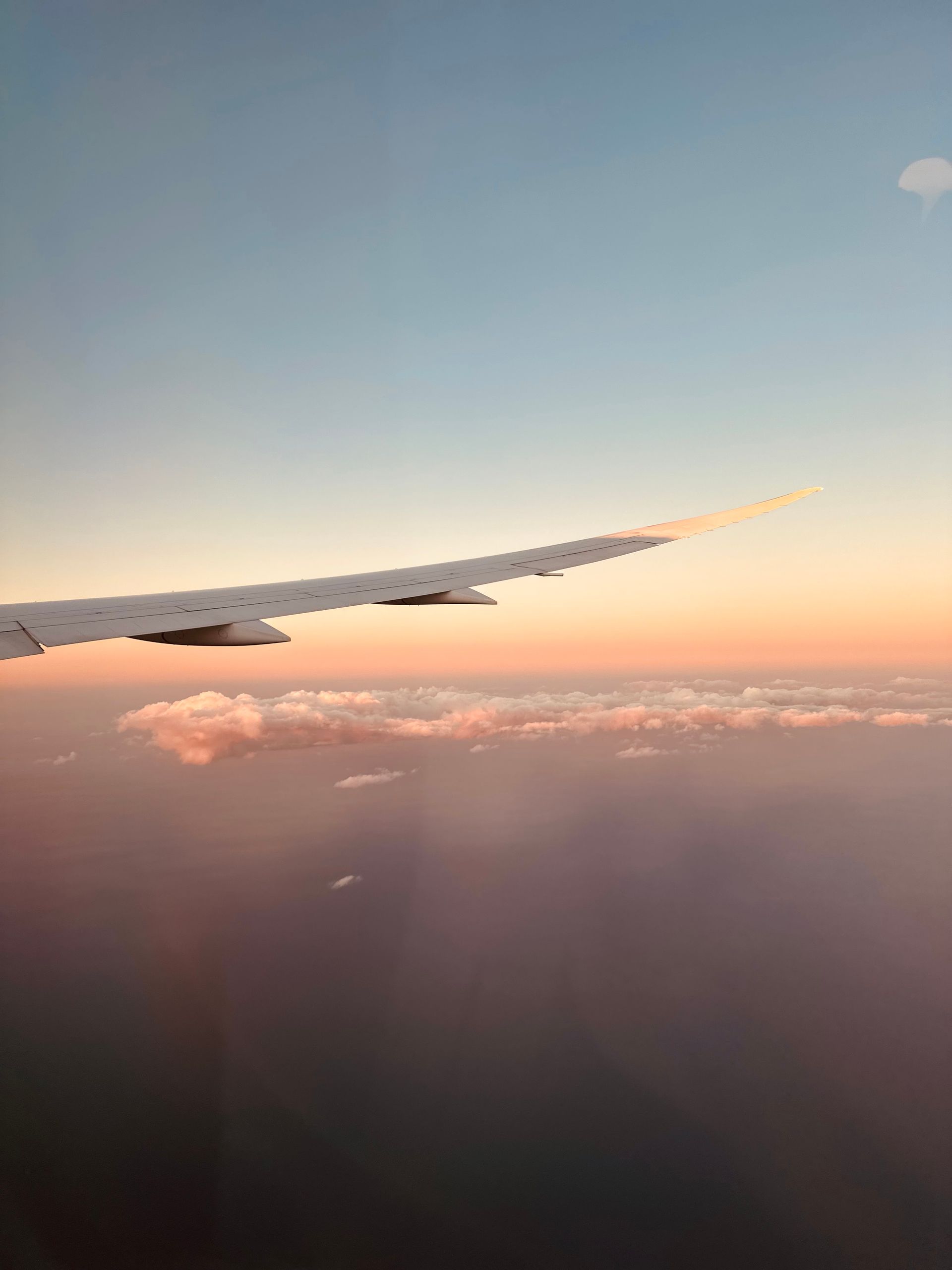 Uitzicht vanuit een vliegtuigraam tijdens zonsondergang:vleugel boven de wolken met zacht roze gloed
