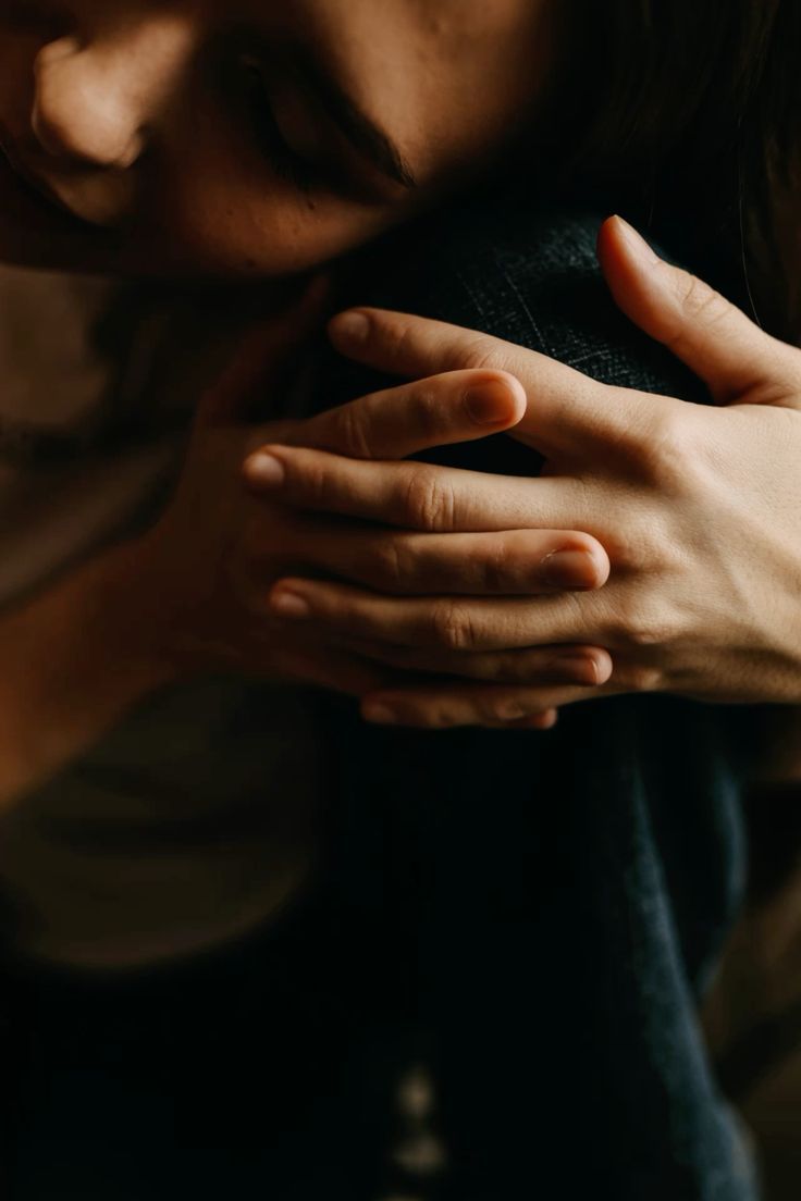 A close-up view of hands gently embracing a shoulder, conveying comfort and support in soft, dim lighting.