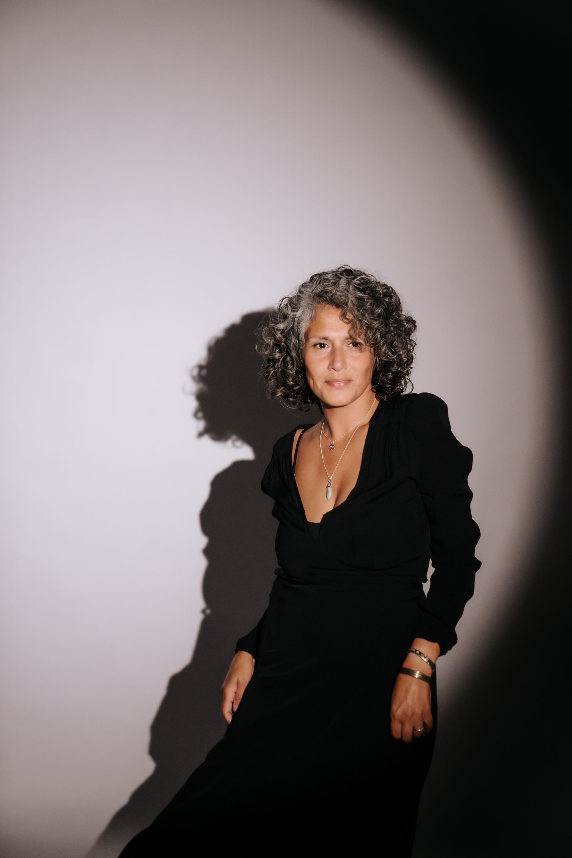 Vrouw in zwarte jurk voor een witte muur – symbool voor kracht, zelfbewustzijn en innerlijke balans.