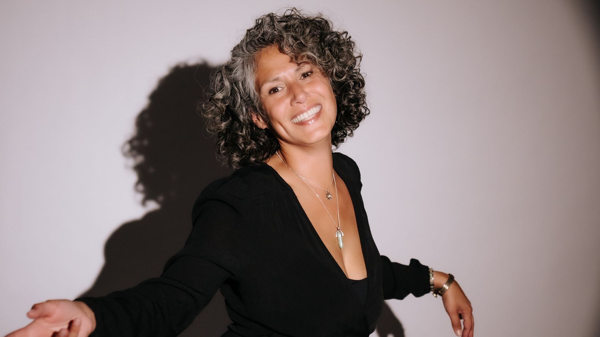 Vrouw in zwarte jurk voor een witte muur – symbool voor kracht, zelfbewustzijn en innerlijke balans.