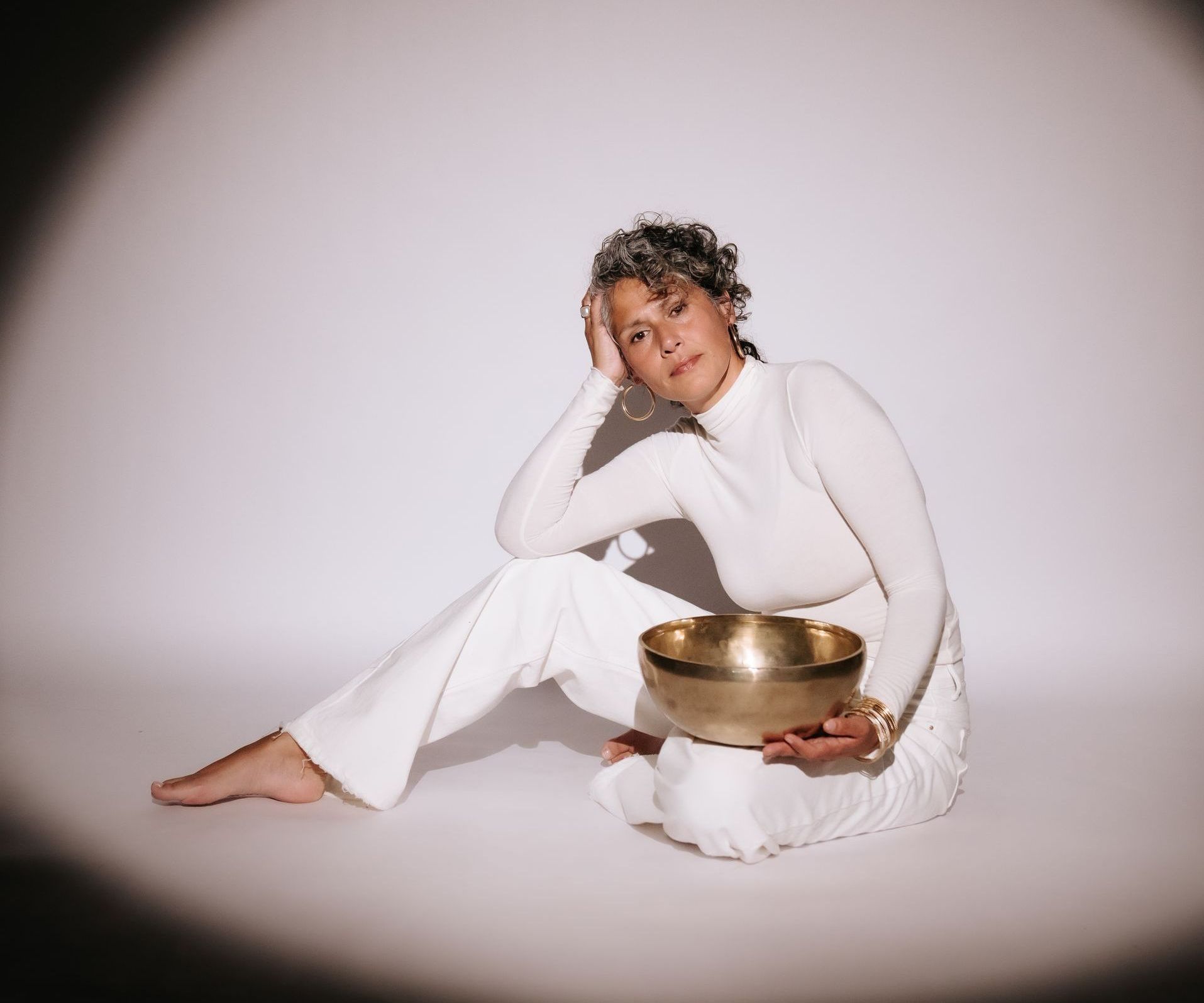 Vrouw in witte kleding speelt op een klankschaal, met een zachte glimlach en warme spotlight.