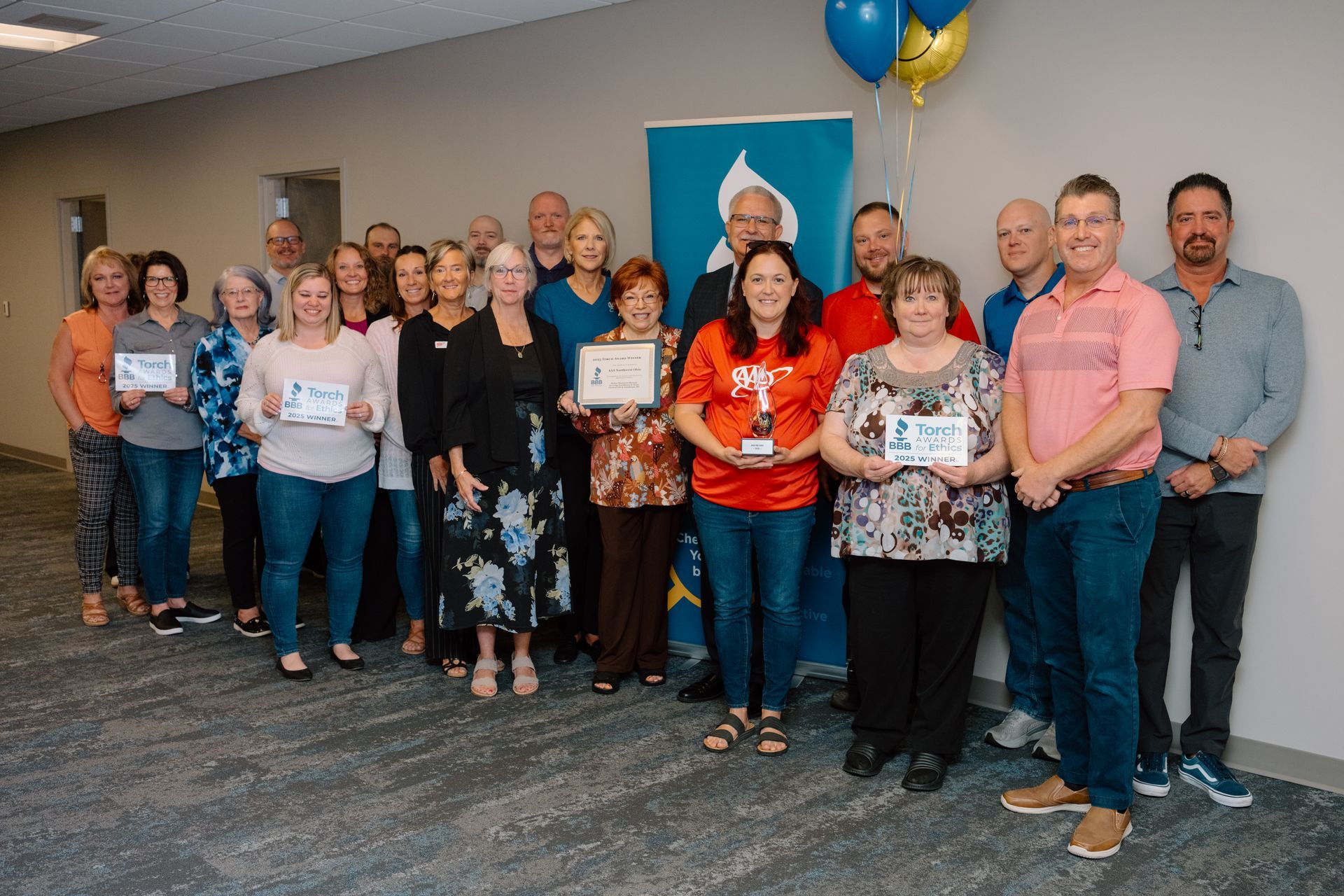 Group of people holding Torch award, smiling near a banner and balloons in an office.