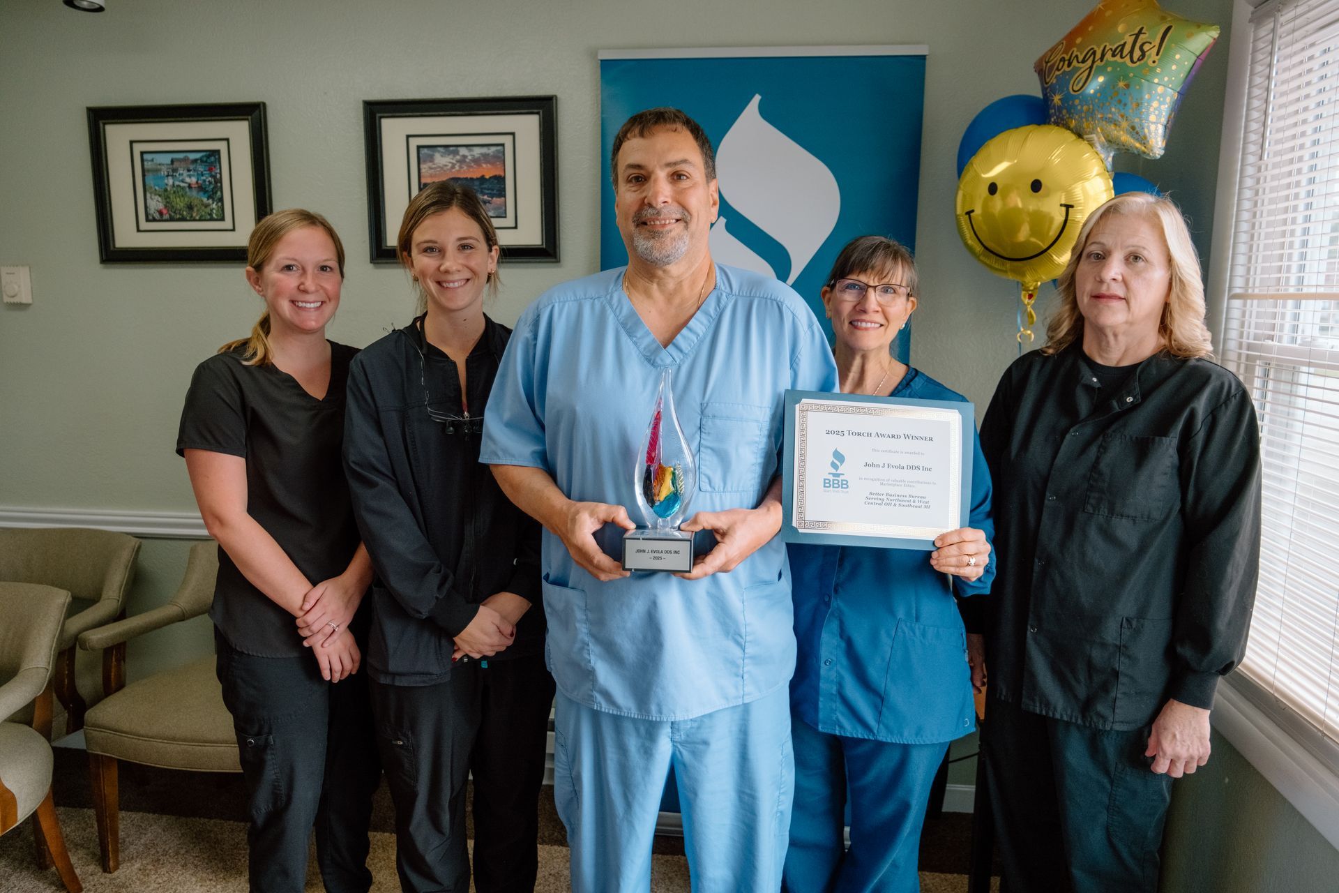 A dental team celebrates, holding an award and certificate in a bright office.