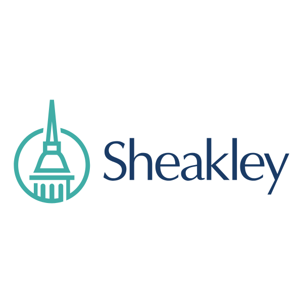 Logo for Sheakley, featuring a teal-colored stylized building within a circle, and the company name in dark blue text.