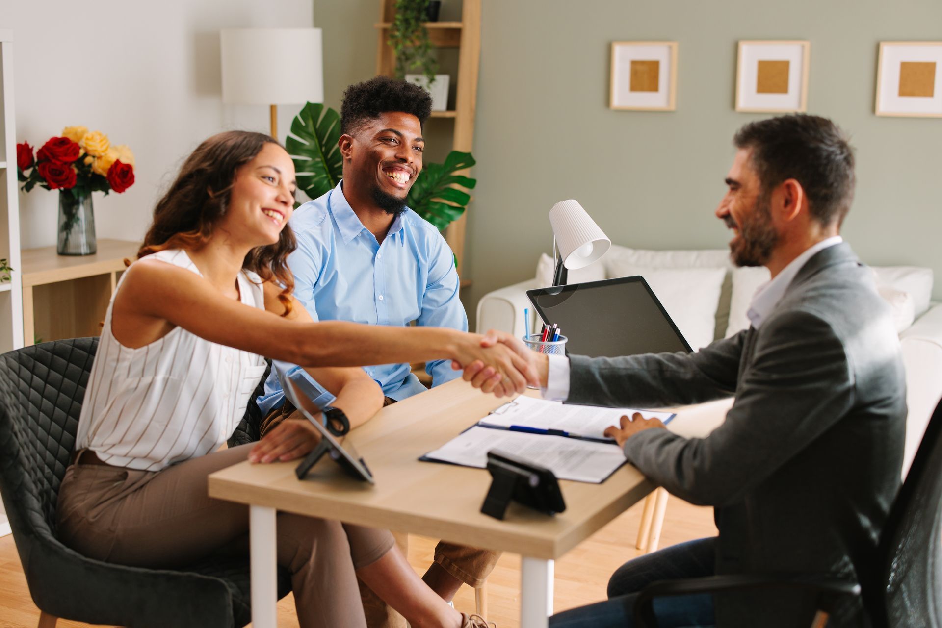 Couple shaking hands with a professional at a desk. Smiling. Indoors.