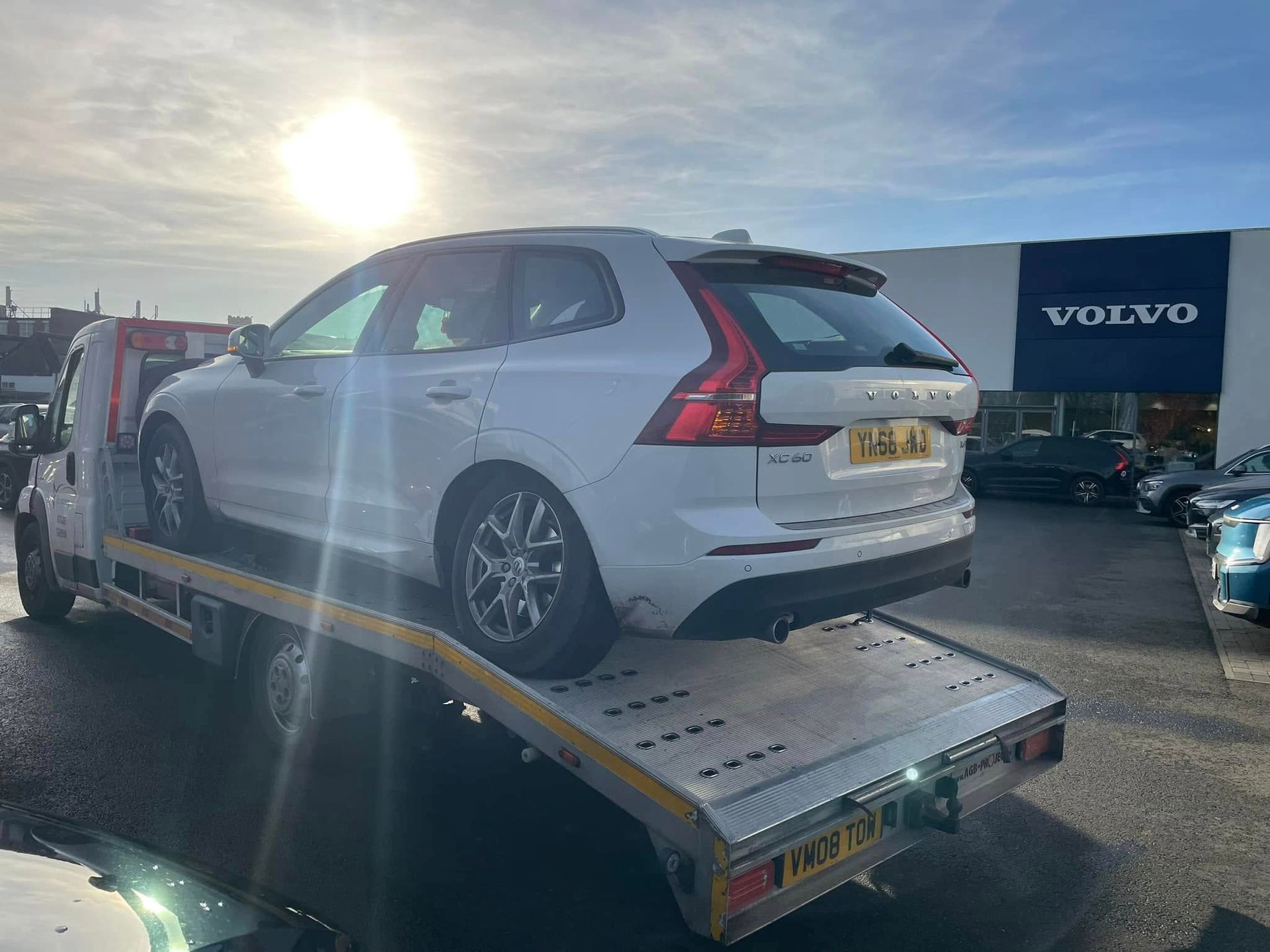 A white volvo is being towed by a tow truck.