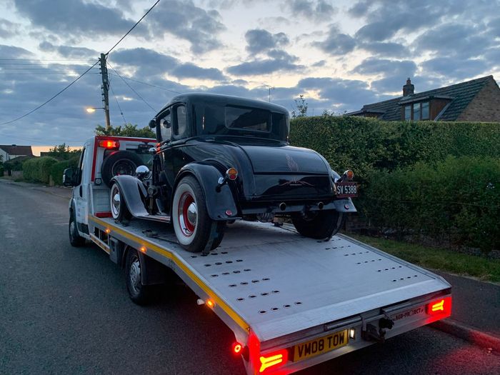 An old black car is being towed by a tow truck.