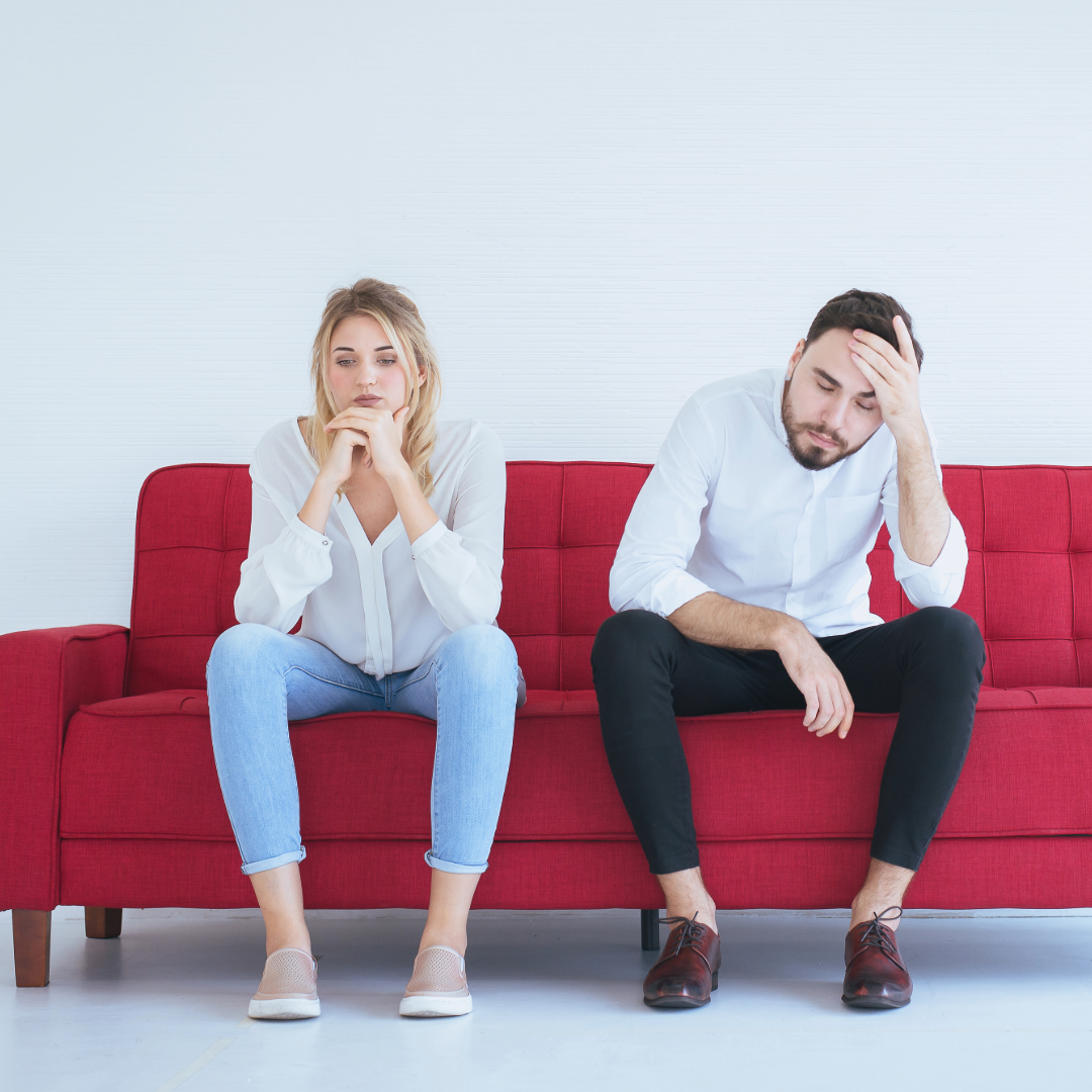 A man and a woman are sitting on a red couch looking at each other.